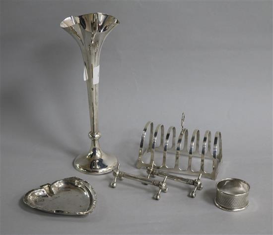 A small group of silver including a toast rack, posy vase, counter dish and a pair of knife rests and napkins ring.